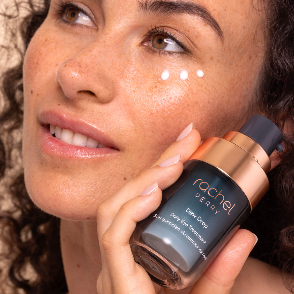 Woman applying natural daily eye treatment skincare product labeled 'Dew Drop' by Rachel Perry to her face