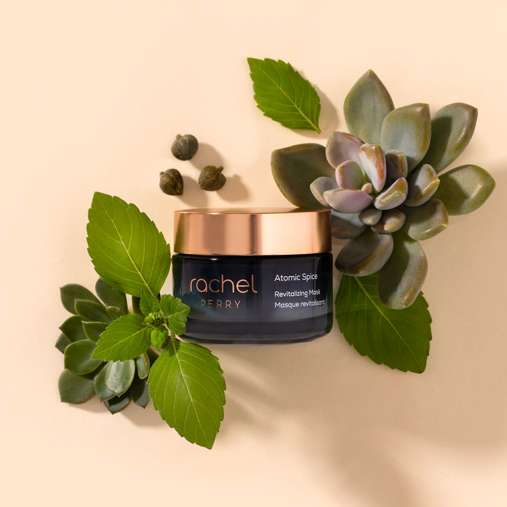 natural skincare jar labeled rachel perry atomic spice revitalizing face mask with succulents and leaves on a beige background