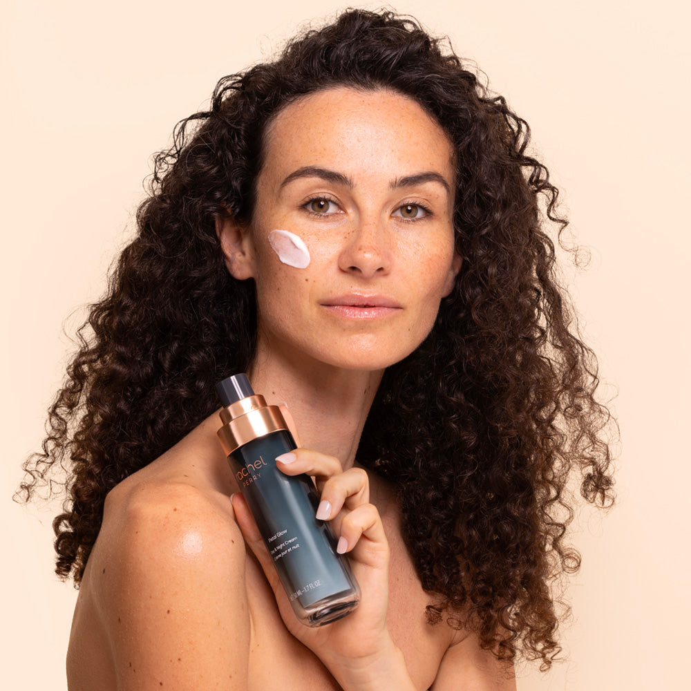 Woman applying natural skincare face moisturizer day night cream with a rachel perry bottle on a beige background